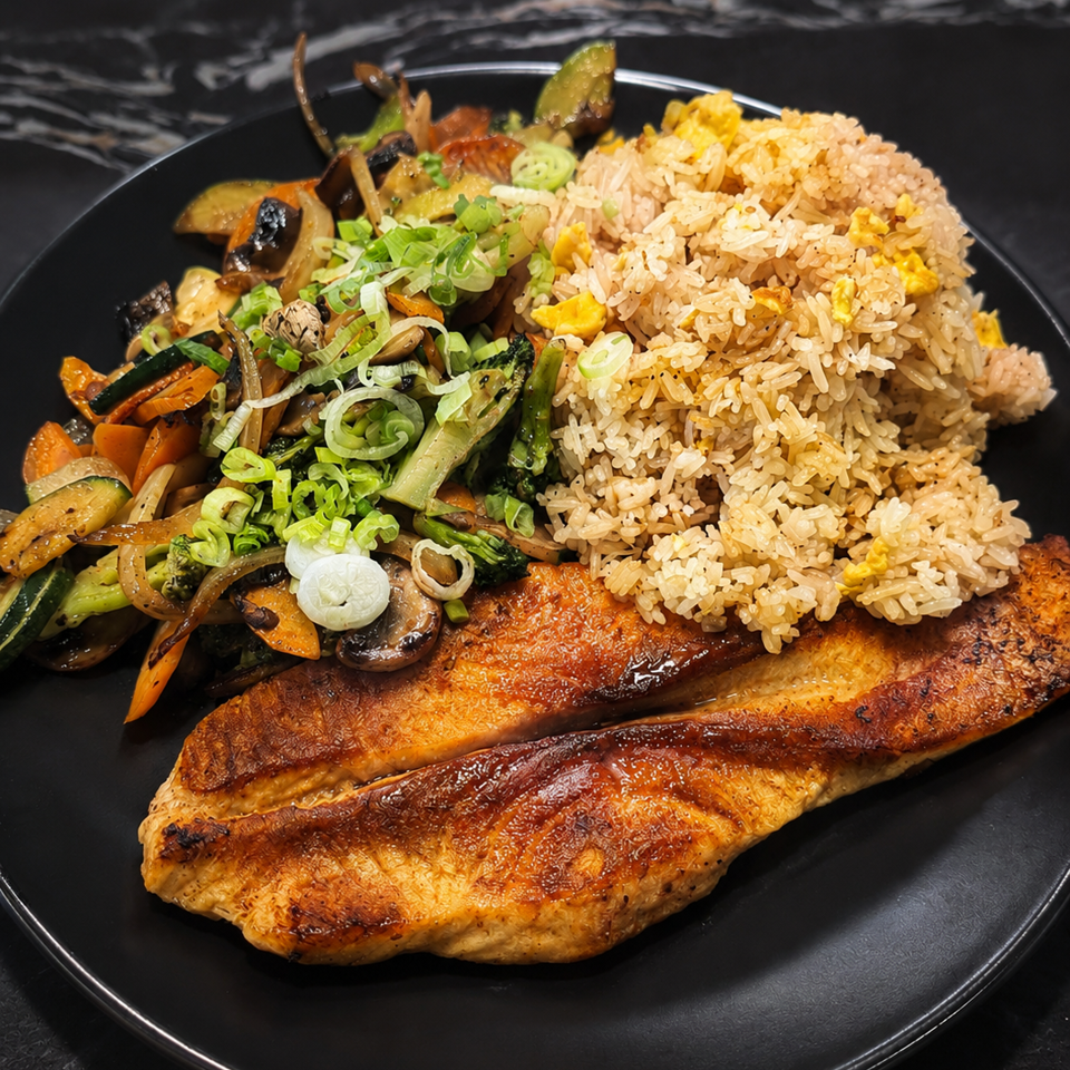 Grilled salmon fillets served with egg fried rice, sautéed mixed vegetables, mushrooms, and sliced green onions on a black plate.